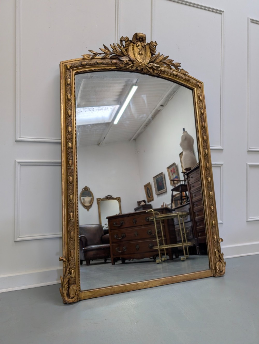 A large nineteenth-century French gilded mirror featuring an arched frame topped with an intricate ribbon crest and beaded border moulding.