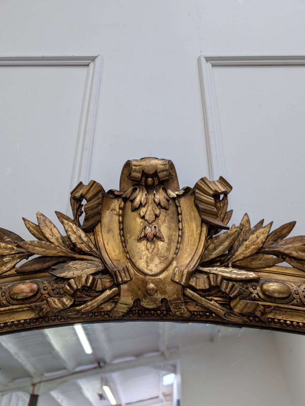 A large nineteenth-century French gilded mirror featuring an arched frame topped with an intricate ribbon crest and beaded border moulding. View V