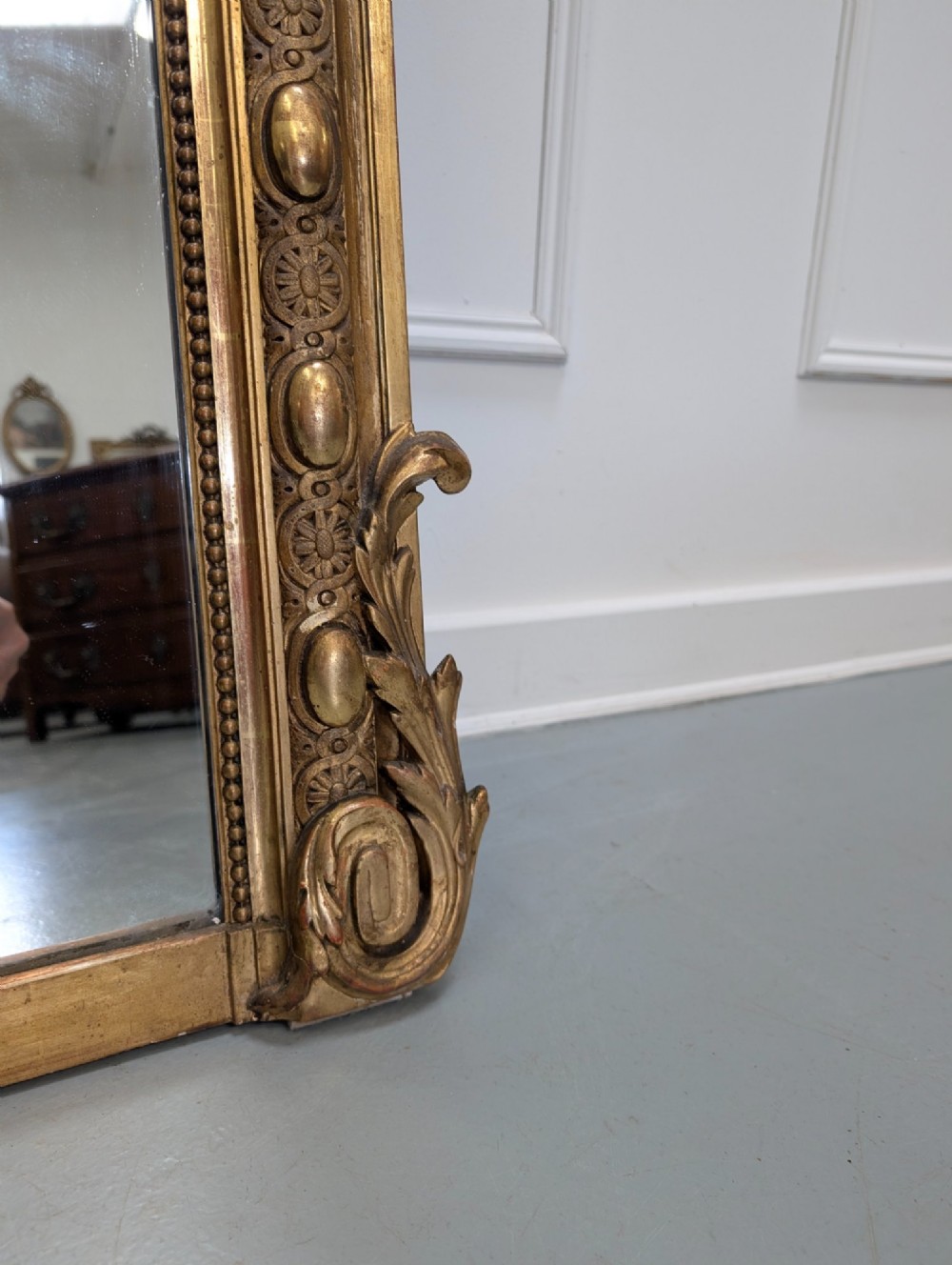 A large nineteenth-century French gilded mirror featuring an arched frame topped with an intricate ribbon crest and beaded border moulding. View VI