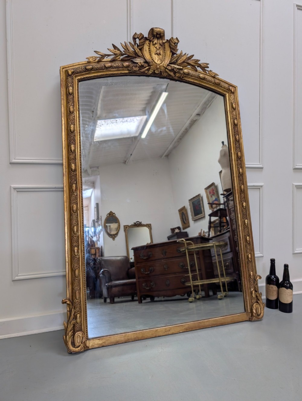 A large nineteenth-century French gilded mirror featuring an arched frame topped with an intricate ribbon crest and beaded border moulding. View VIII