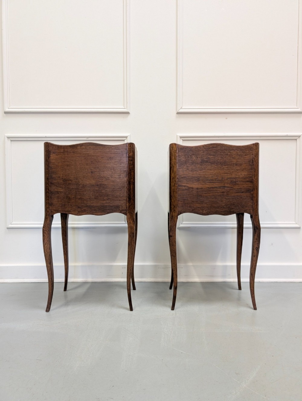 A pair of French dark oak bedside tables featuring slender cabriole legs, an open shelf alcove, and a single drawer with a metal knob. View IV