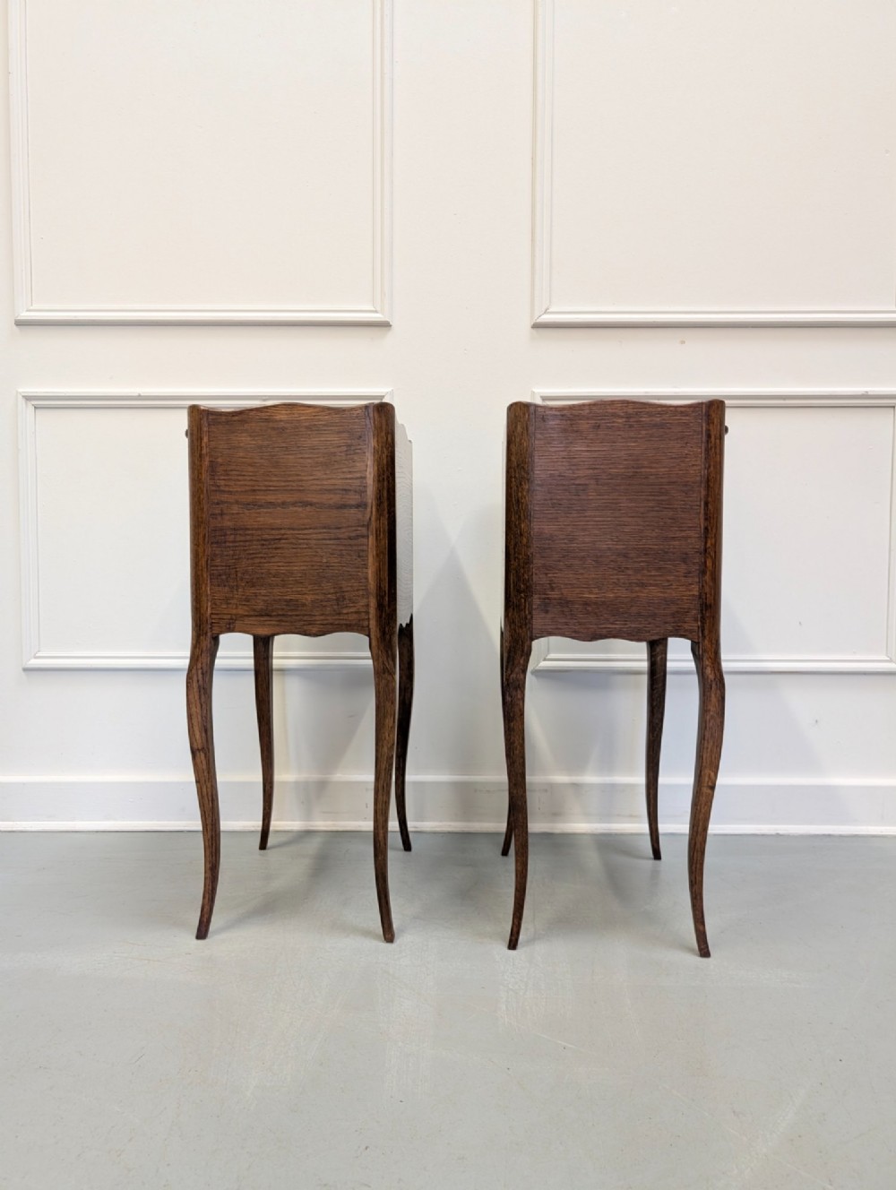 A pair of French dark oak bedside tables featuring slender cabriole legs, an open shelf alcove, and a single drawer with a metal knob. View V