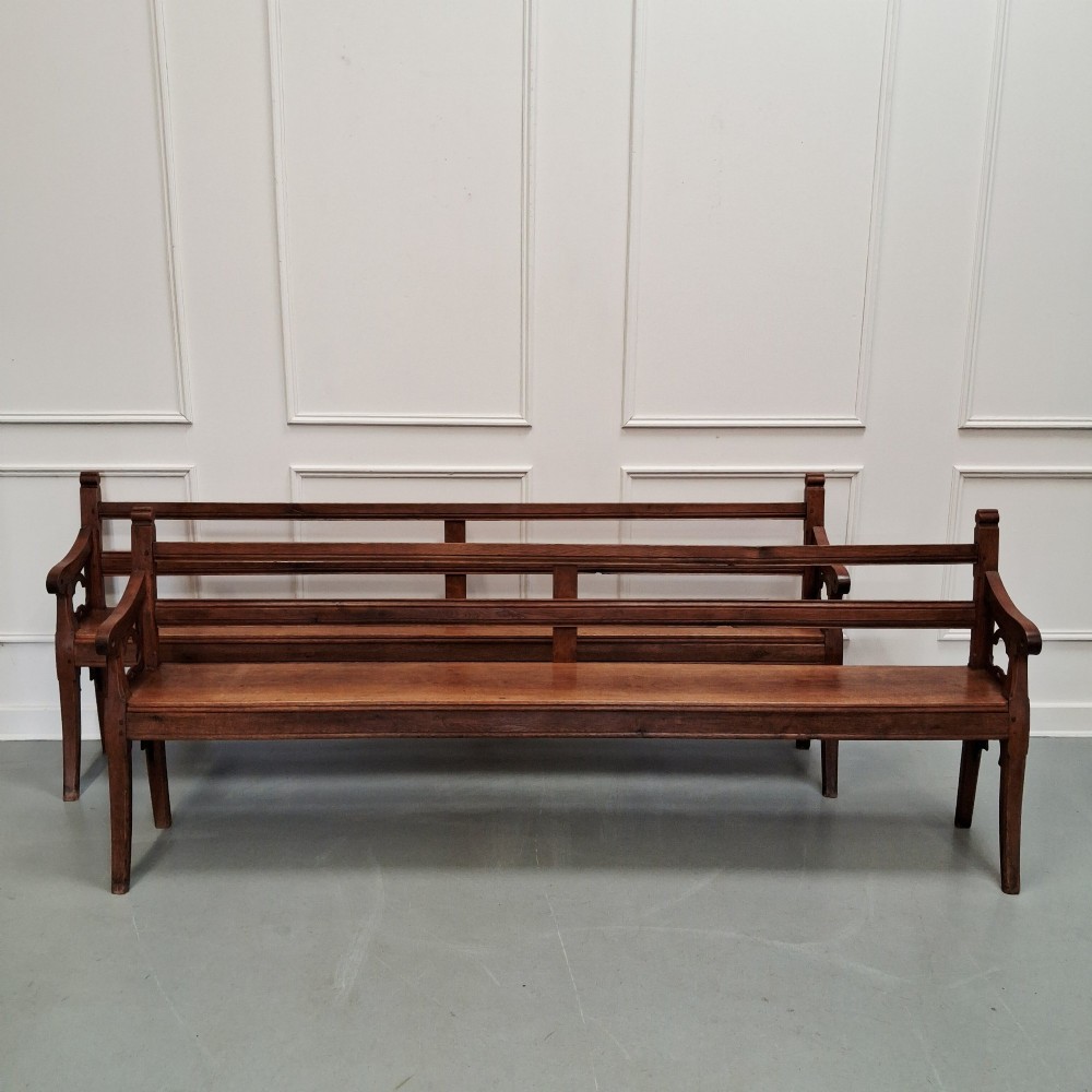 Profile view of a pair of antique Gothic Revival solid oak gallery benches featuring carved trefoil motifs and curved armrests. View III