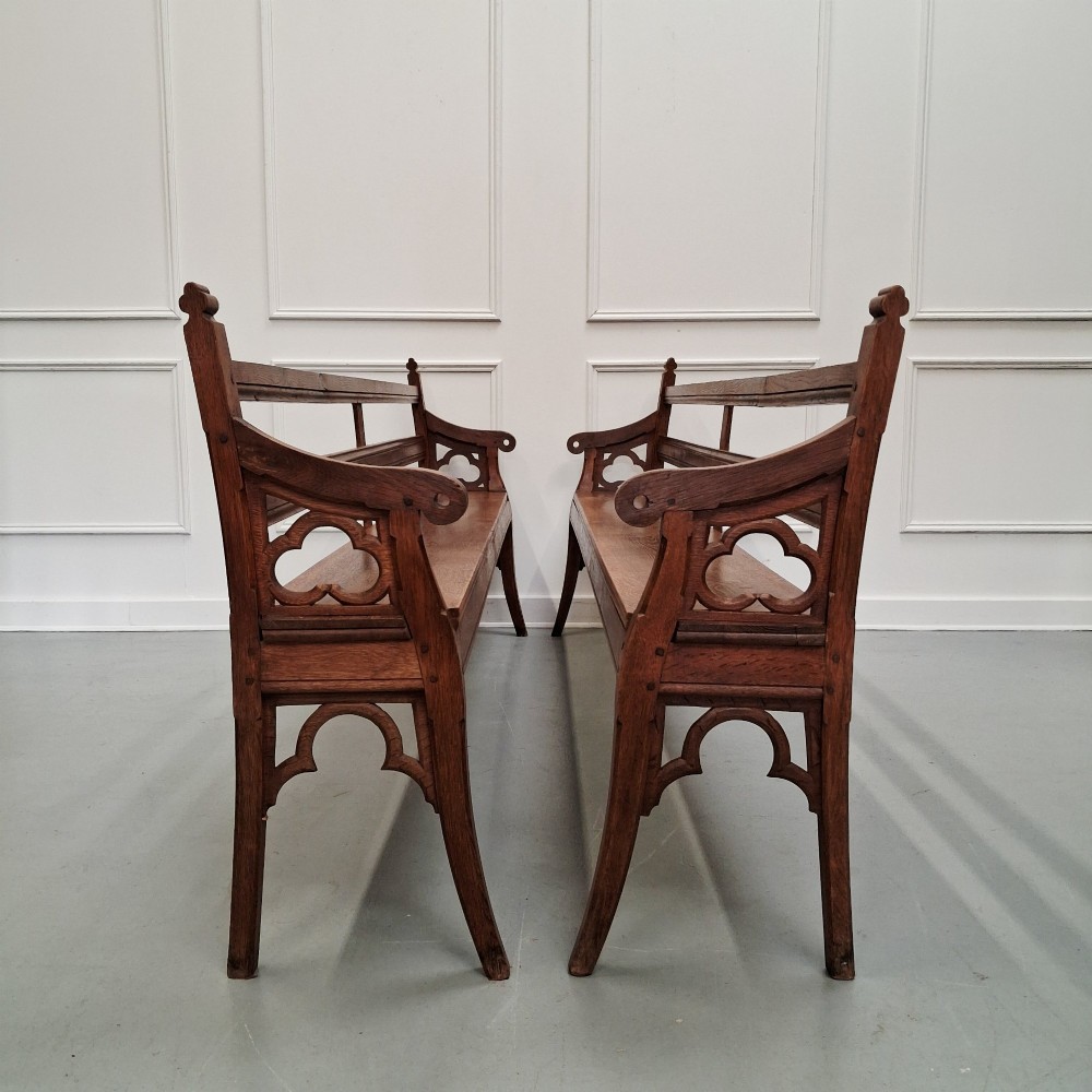 Profile view of a pair of antique Gothic Revival solid oak gallery benches featuring carved trefoil motifs and curved armrests. View IV
