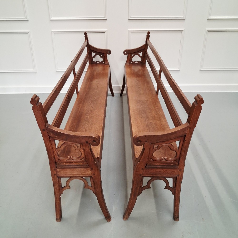 Profile view of a pair of antique Gothic Revival solid oak gallery benches featuring carved trefoil motifs and curved armrests. View V