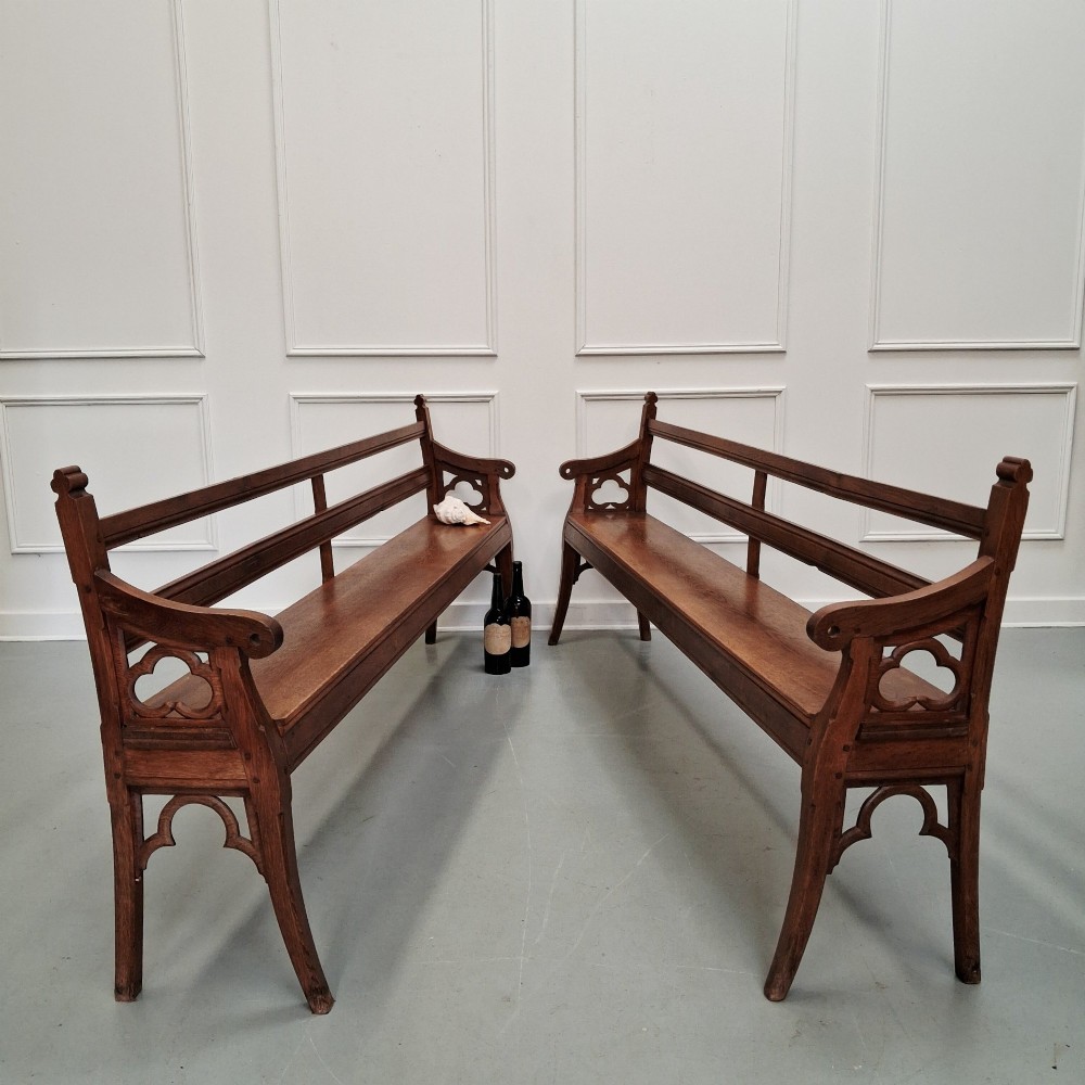 Profile view of a pair of antique Gothic Revival solid oak gallery benches featuring carved trefoil motifs and curved armrests. View VI
