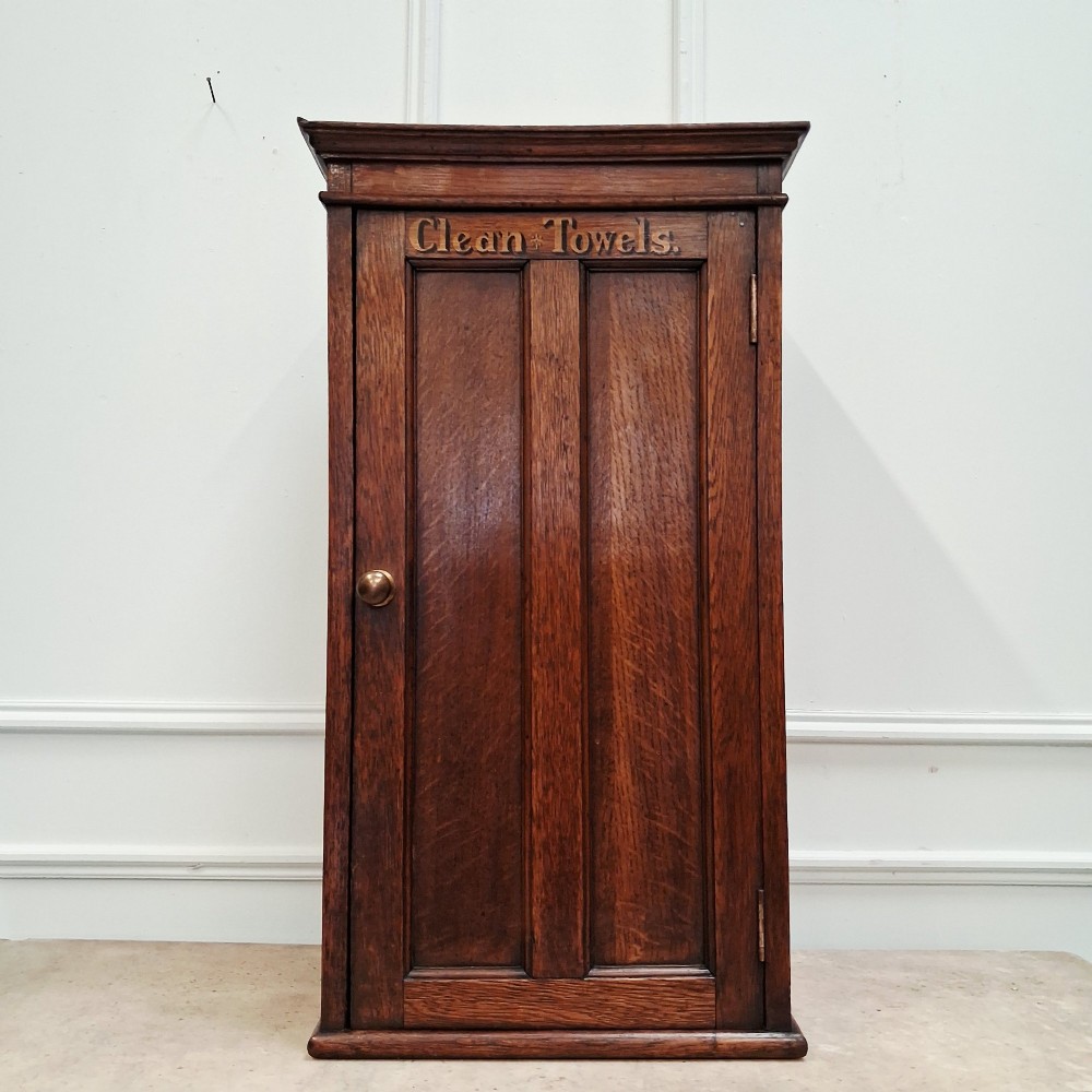 An antique medium brown oak wall cupboard featuring a panelled single door with Clean Towels in gilt lettering across the top and a brass door knob.
