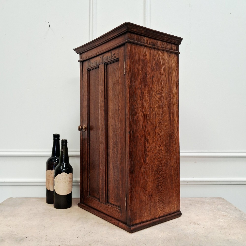 An antique medium brown oak wall cupboard featuring a panelled single door with Clean Towels in gilt lettering across the top and a brass door knob. View V