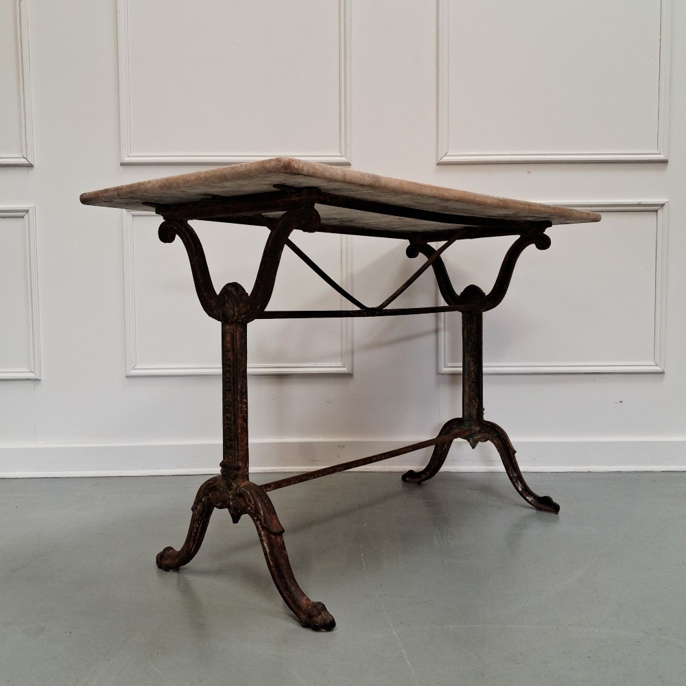 A rectangular off-white marble top bistro table supported by a dark weathered cast iron frame with scrolled legs and stretchers.