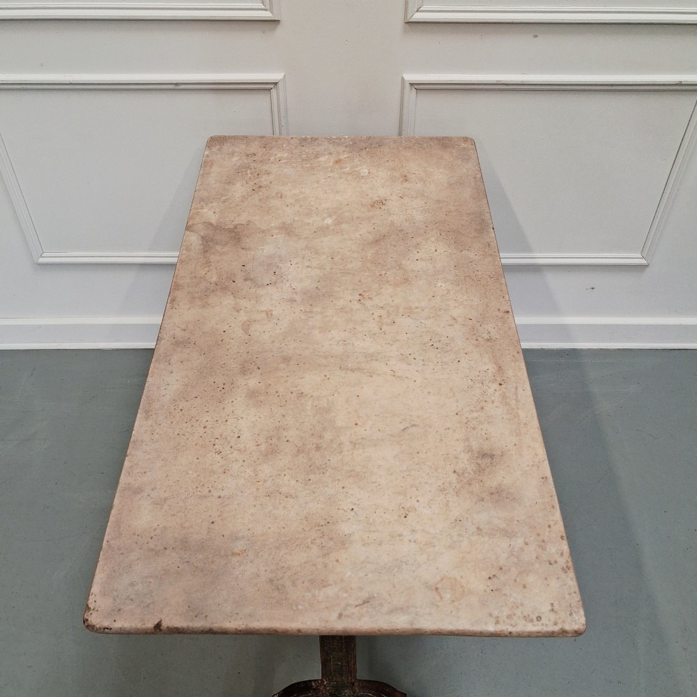 A rectangular off-white marble top bistro table supported by a dark weathered cast iron frame with scrolled legs and stretchers. View II