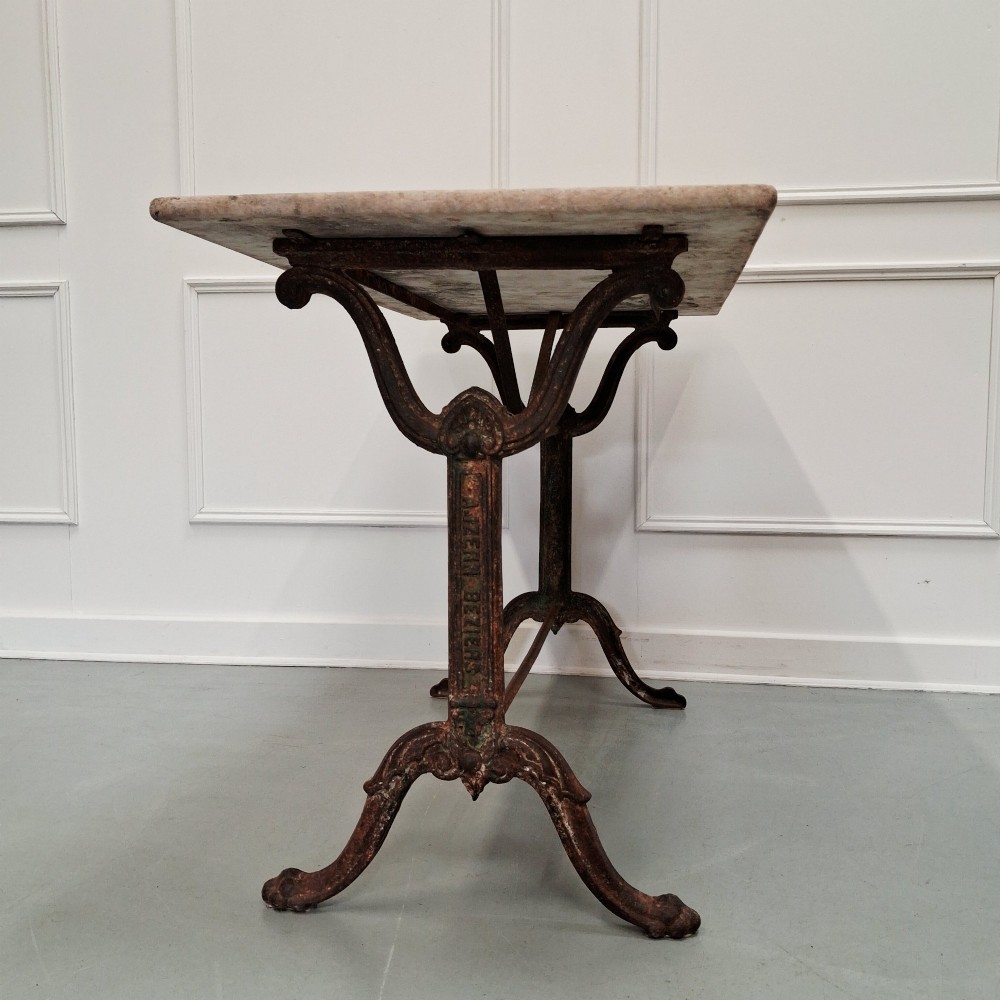 A rectangular off-white marble top bistro table supported by a dark weathered cast iron frame with scrolled legs and stretchers. View IV