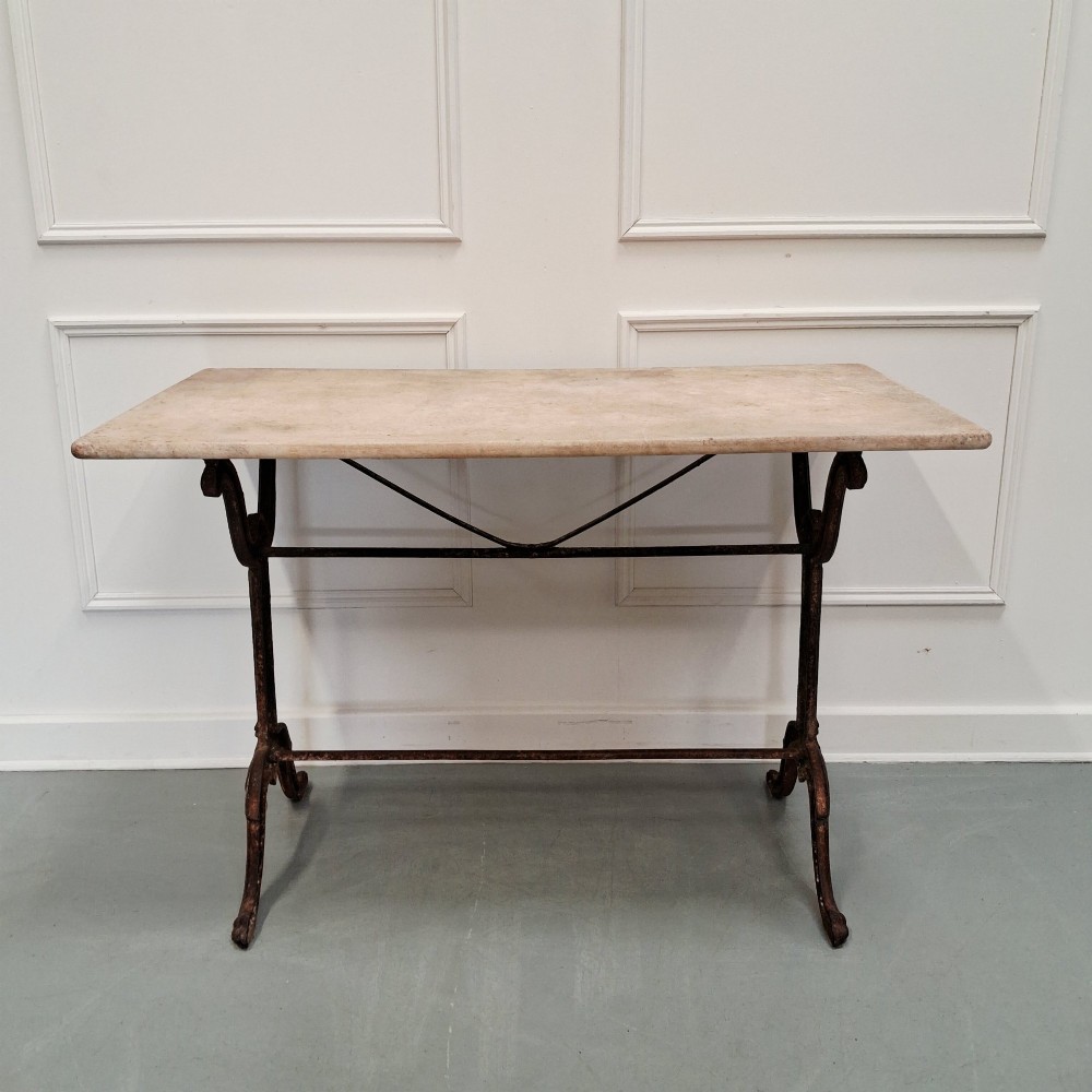 A rectangular off-white marble top bistro table supported by a dark weathered cast iron frame with scrolled legs and stretchers. View VI