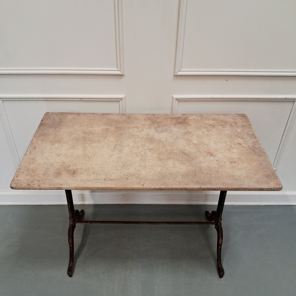 A rectangular off-white marble top bistro table supported by a dark weathered cast iron frame with scrolled legs and stretchers. View VII