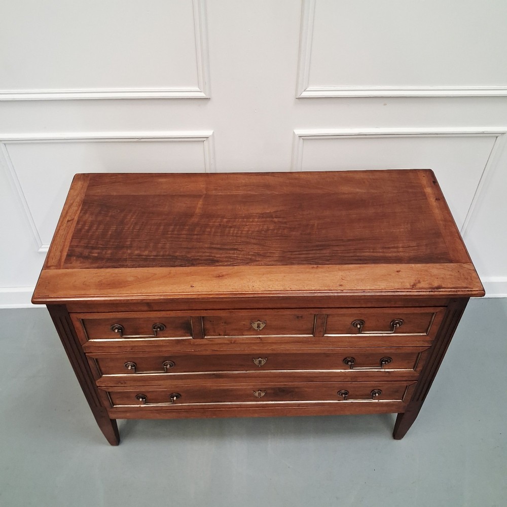 A late 19th-century French walnut commode featuring three drawer tiers, brass handles, shield-shaped escutcheons, and tapered fluted legs. View III