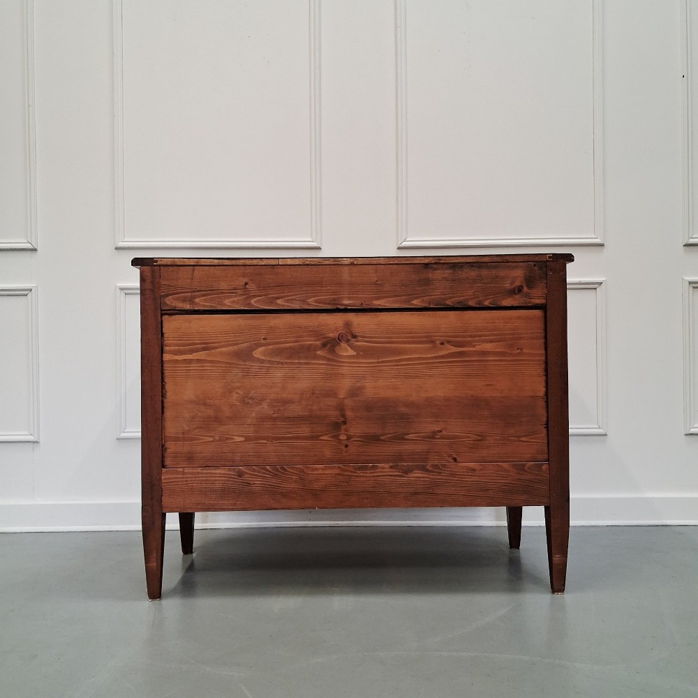 A late 19th-century French walnut commode featuring three drawer tiers, brass handles, shield-shaped escutcheons, and tapered fluted legs. View VII