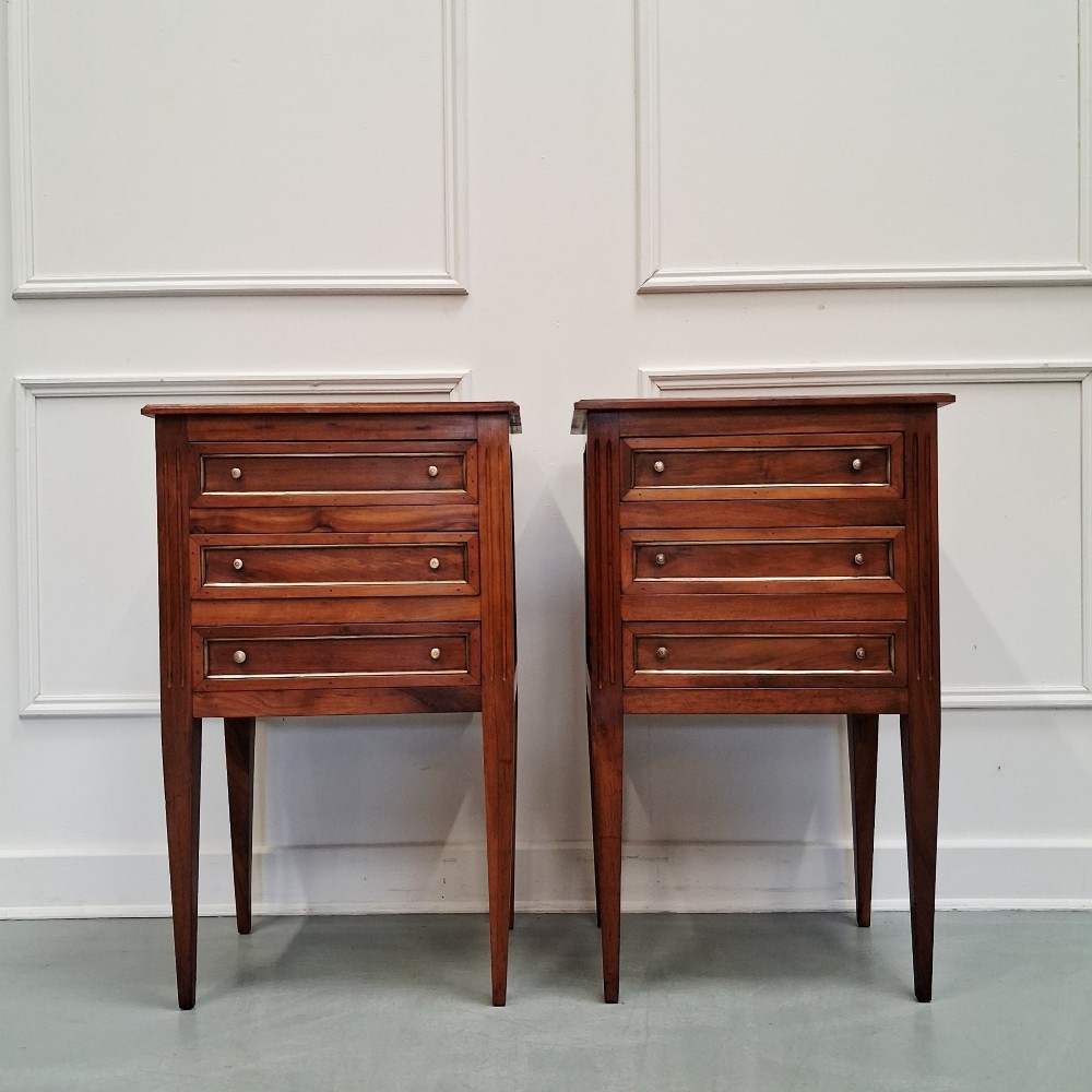 A pair of French antique walnut bedside tables with three drawers and slender tapered legs.