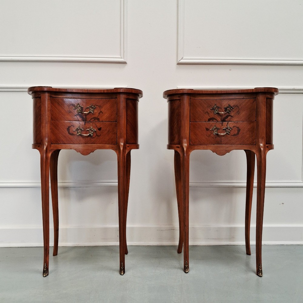A pair of slender French style kingwood bedside cabinets featuring marquetry floral inlay, two drawers with brass handles, and tall cabriole legs.