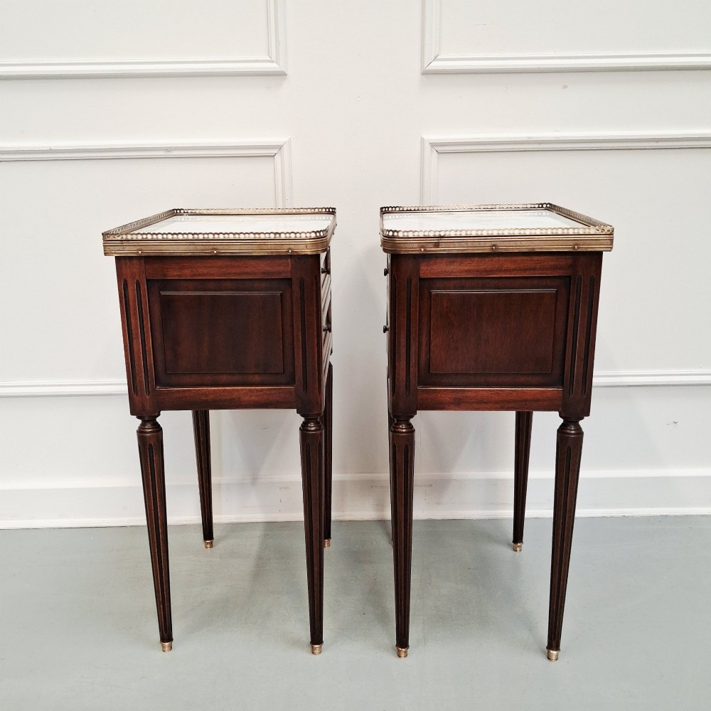 A pair of slim dark wood French bedside tables featuring fluted legs, brass galleries, two drawers, and inset marble tops. View IV