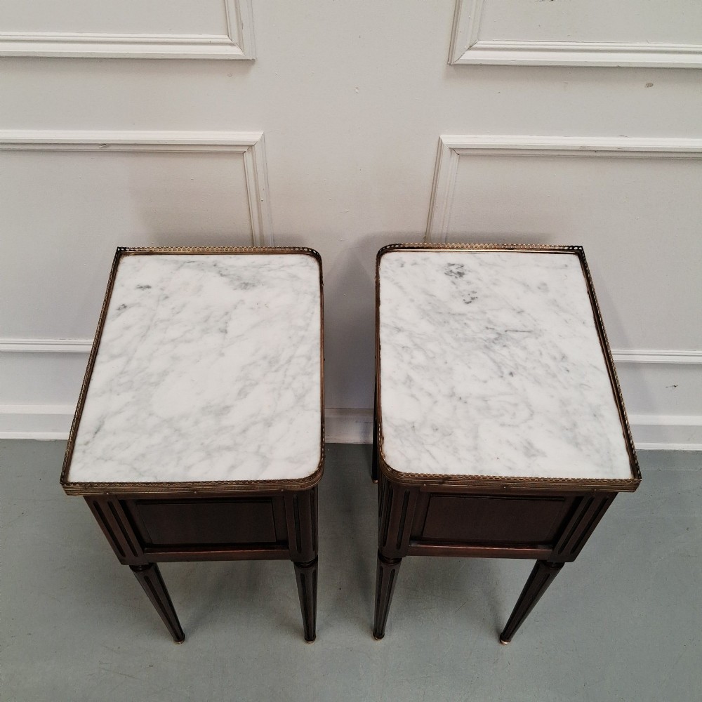 A pair of slim dark wood French bedside tables featuring fluted legs, brass galleries, two drawers, and inset marble tops. View V
