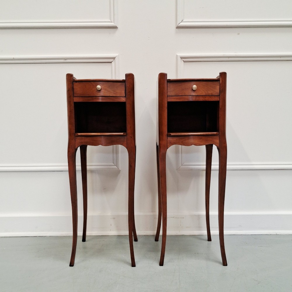 A pair of tall French cherry wood bedside tables featuring single frieze drawers, open compartments, and slender cabriole legs.