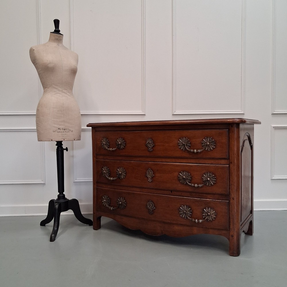 A French country walnut commode featuring three full-width drawers with ornate brass hardware and a scalloped lower apron.