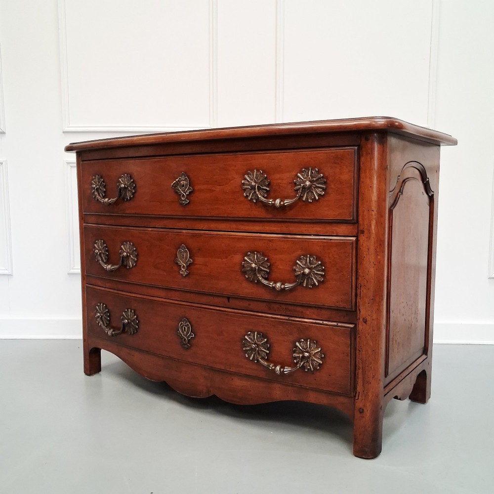 A French country walnut commode featuring three full-width drawers with ornate brass hardware and a scalloped lower apron. View II