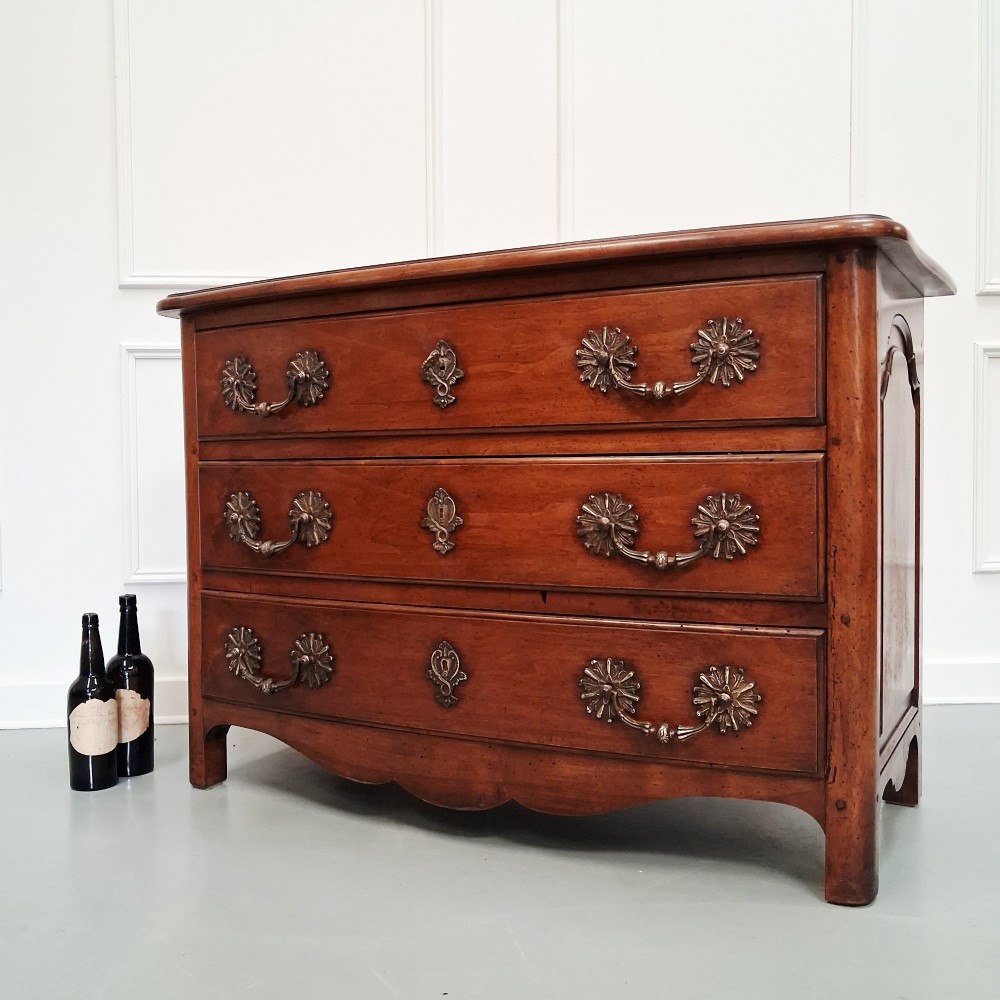 A French country walnut commode featuring three full-width drawers with ornate brass hardware and a scalloped lower apron. View III