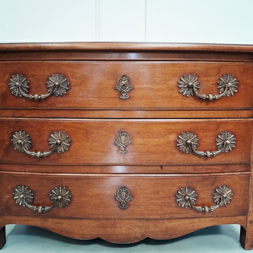 A French country walnut commode featuring three full-width drawers with ornate brass hardware and a scalloped lower apron. View IV