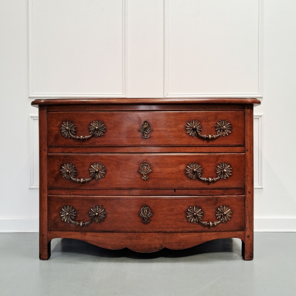 A French country walnut commode featuring three full-width drawers with ornate brass hardware and a scalloped lower apron. View V