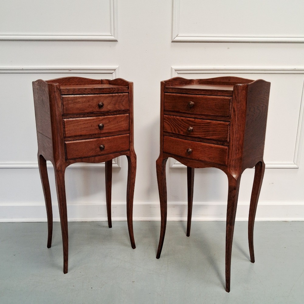 A matching pair of tall French oak bedside tables with slender cabriole legs, three drawers each, and metal knobs.