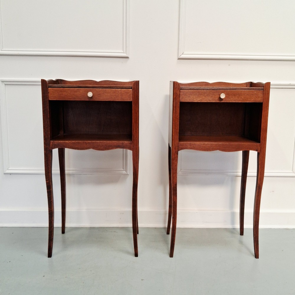A pair of tall French oak bedside tables featuring single top drawers, open storage alcoves, scalloped aprons, and slender curved cabriole legs.