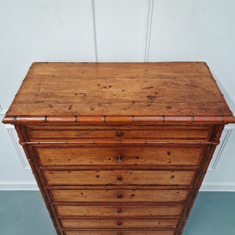 A tall 19th-century French wooden semainier chest featuring seven drawers framed by turned faux bamboo mouldings and supported by bun feet. View III