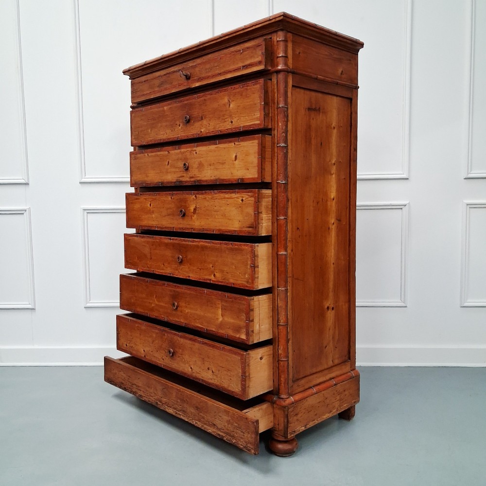 A tall 19th-century French wooden semainier chest featuring seven drawers framed by turned faux bamboo mouldings and supported by bun feet. View X