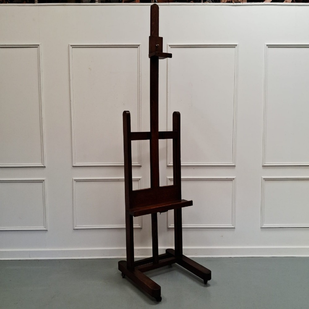 A dark oak French studio easel from circa 1890 featuring an adjustable vertical shaft, horizontal support shelf, and caster feet.