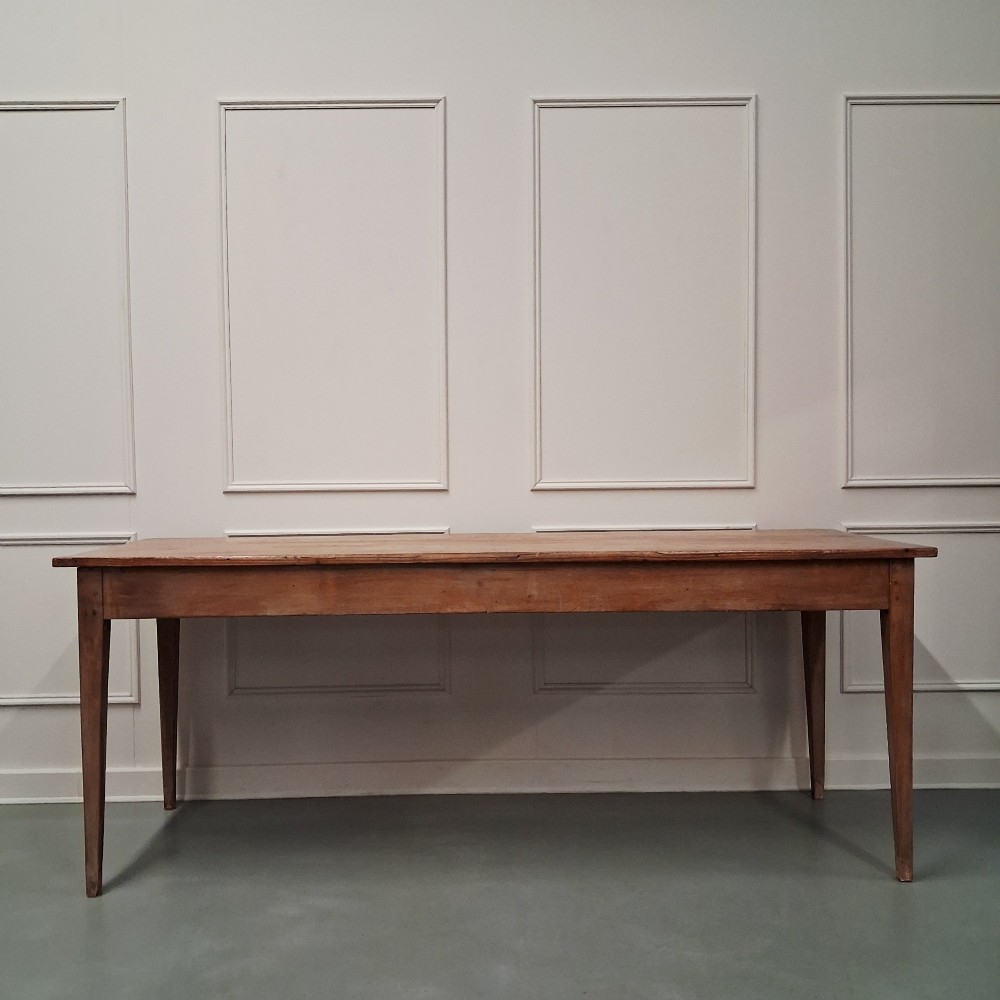 A long antique pine dining table featuring a solid plank top, deep side apron, and four tapered square legs.
