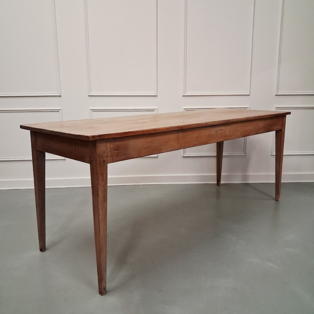 A long antique pine dining table featuring a solid plank top, deep side apron, and four tapered square legs. View V