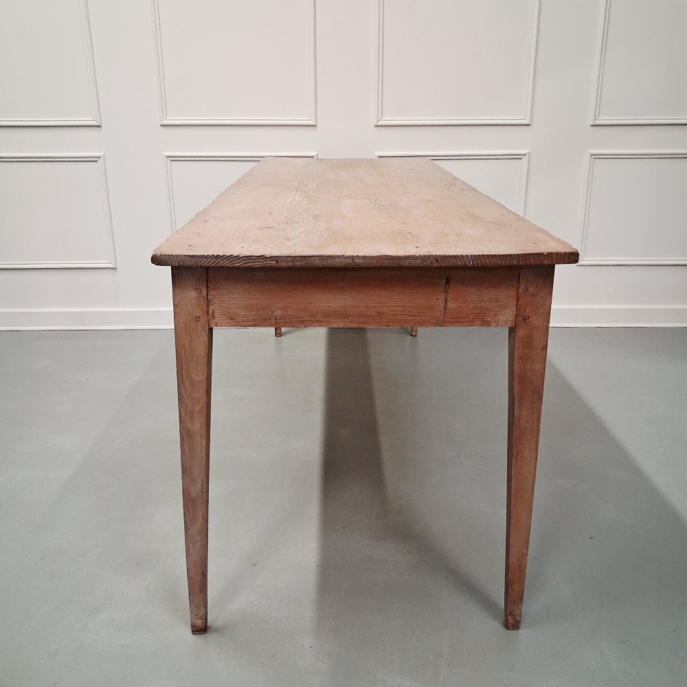 A long antique pine dining table featuring a solid plank top, deep side apron, and four tapered square legs. View VII