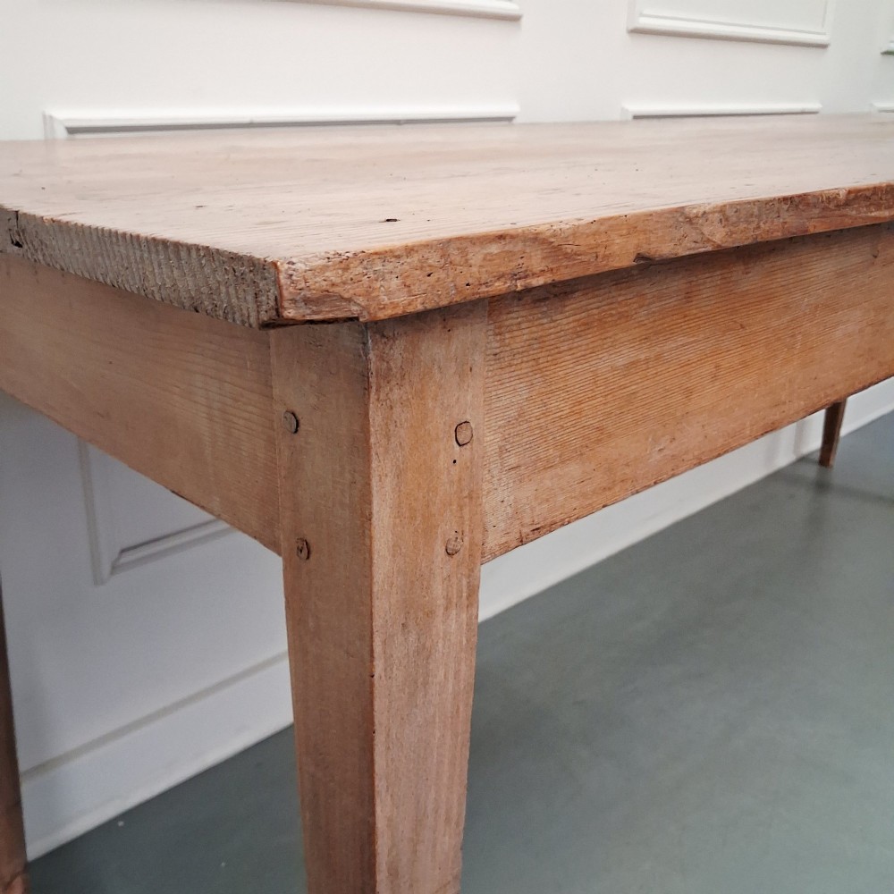 A long antique pine dining table featuring a solid plank top, deep side apron, and four tapered square legs. View XI
