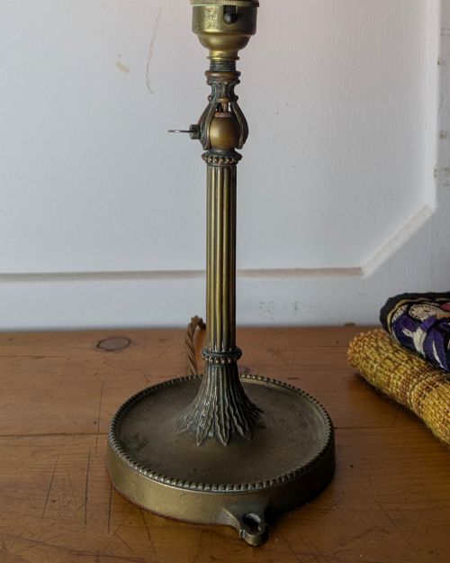 fig 2. A slim early 20th-century aged brass lamp featuring a fluted stem, circular base, socket switch, and an exposed filament bulb.