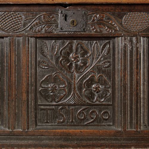 fig 1. A dark oak panelled chest featuring detailed floral and foliage relief carvings, a central panel inscribed TS 1690, and an iron lockplate.