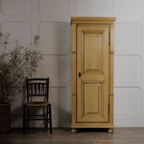 fig 1. A tall single door stripped pine armoire featuring fielded panels, fluted side pilasters, and turned bun feet.
