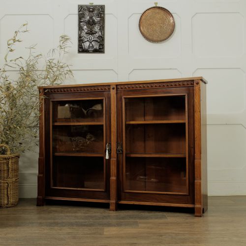 fig 1. An early 20th-century low double-section wooden bookcase featuring glazed doors with carved diamond border trim and three internal shelf levels filled with books.