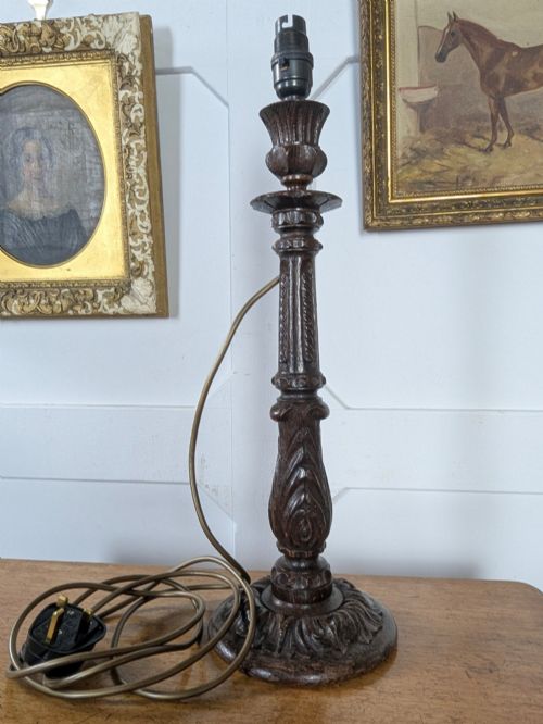 fig 1. A late Victorian carved dark oak candlestick table lamp base featuring detailed acanthus leaf carvings and an exposed filament bulb.