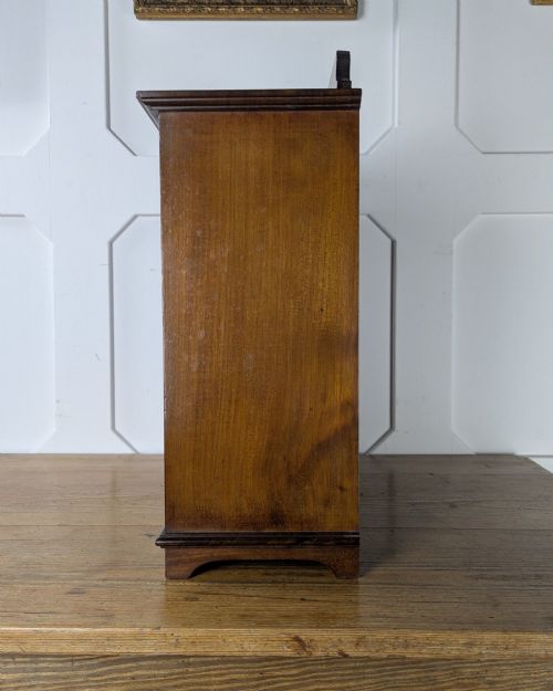 fig 2. A late nineteenth-century warm brown wooden smokers cabinet featuring an open shelf over two drawers on the left, a single inlaid door on the right, and brass hardware.