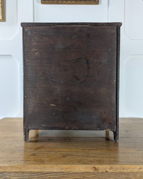 fig 3. A 19th-century miniature wooden chest of drawers with a dark stained finish, two small top drawers over three long drawers, turned knobs, and brass escutcheons.