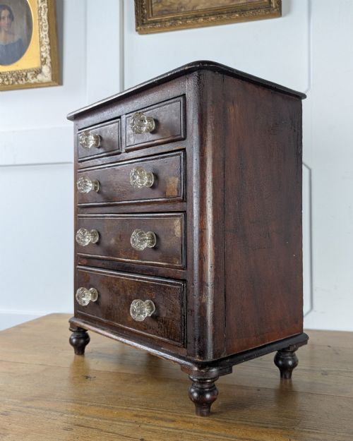 fig 1. A dark brown Victorian miniature wooden chest of drawers with glass knobs and small turned feet.