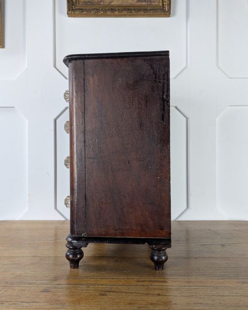 fig 2. A dark brown Victorian miniature wooden chest of drawers with glass knobs and small turned feet.