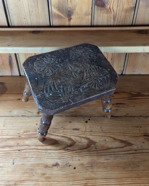fig 1. A dark oak 19th-century rectangular wooden stool featuring hand-carved rosette motifs on the seat top and four turned legs.