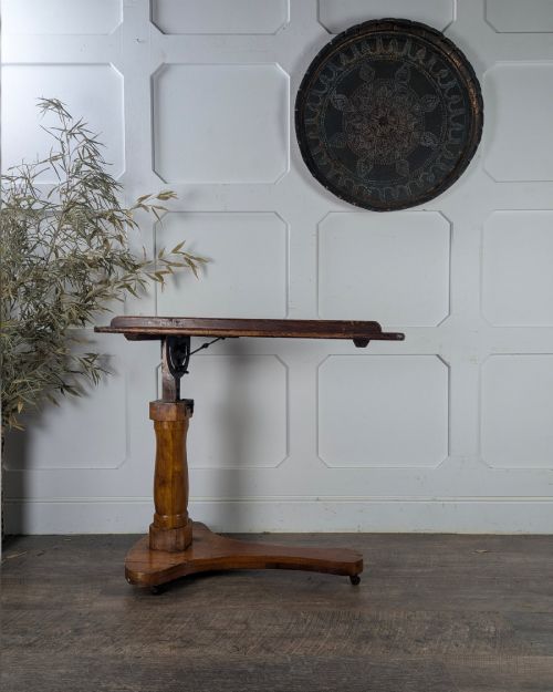 fig 1. An early 20th-century pine reading table featuring an adjustable tilting top, a central turned support column, and a shaped base on small castors.