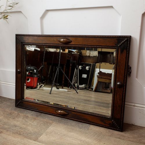 fig 1. A rectangular dark oak wall mirror featuring a bevelled glass plate, beaded moulding around the frame, and applied wooden boss embellishments.